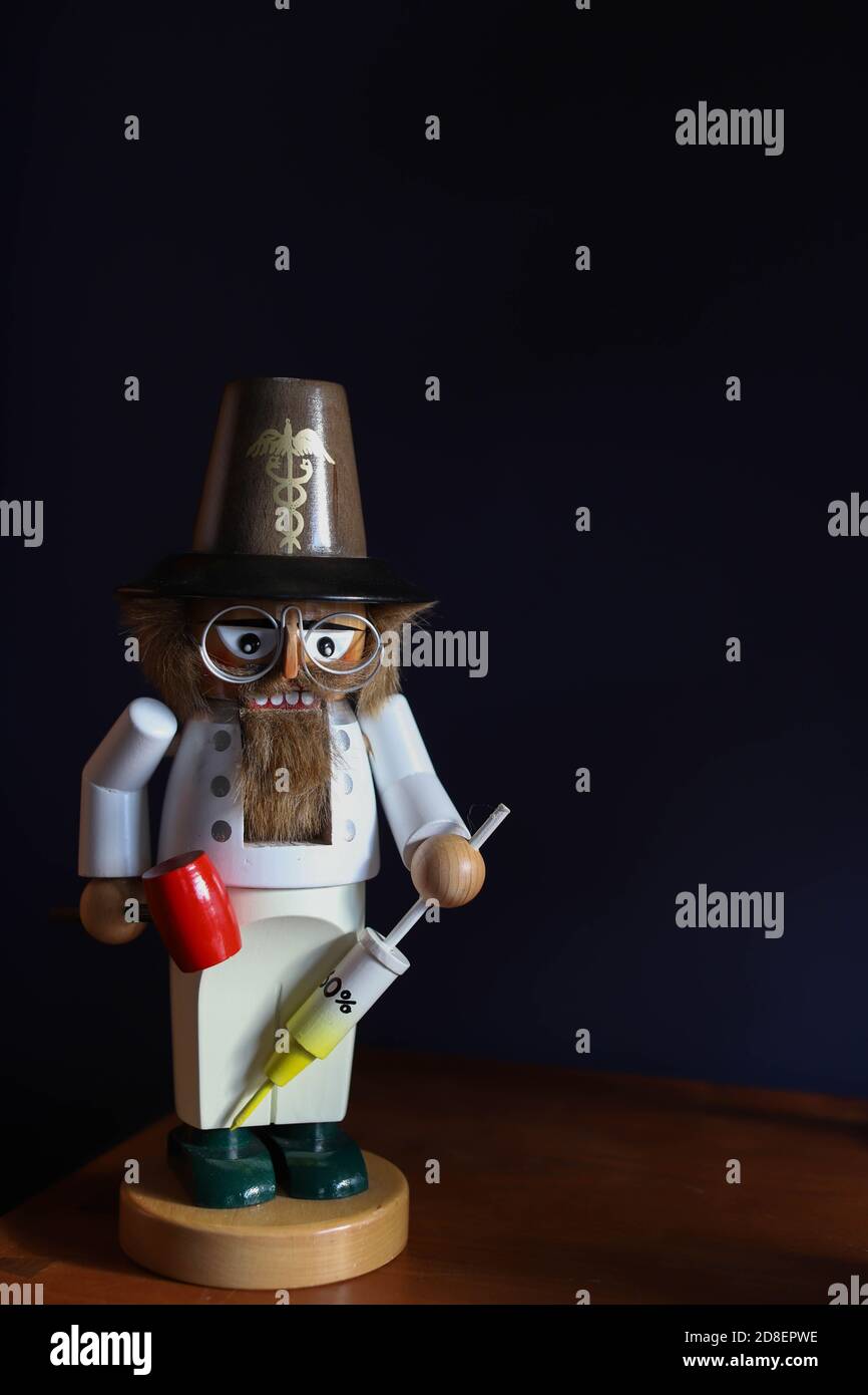 Un nutcracker di legno antico vestito come un medico che tiene un siringa e martello a riflessione Foto Stock