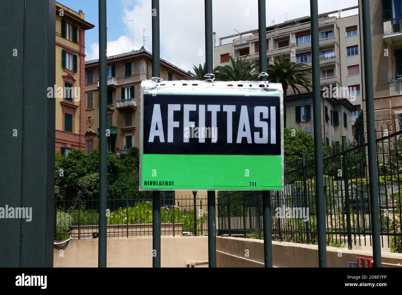Immobiliare in affitto cartello verde su cancello di fronte ad un gruppo di edifici residenziali in Italia. Segno italiano 'Affittasi' traduzione di 'in affitto' Foto Stock
