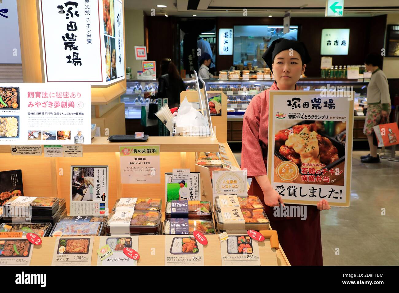 Una giovane donna che lavora per una bancarella di cibo che tiene un Tabellone pubblicitario per un premiato pasto Bento.Tokyu Food Show.Tokyu Grandi magazzini.Shibuya.Tokyo.Japan Foto Stock