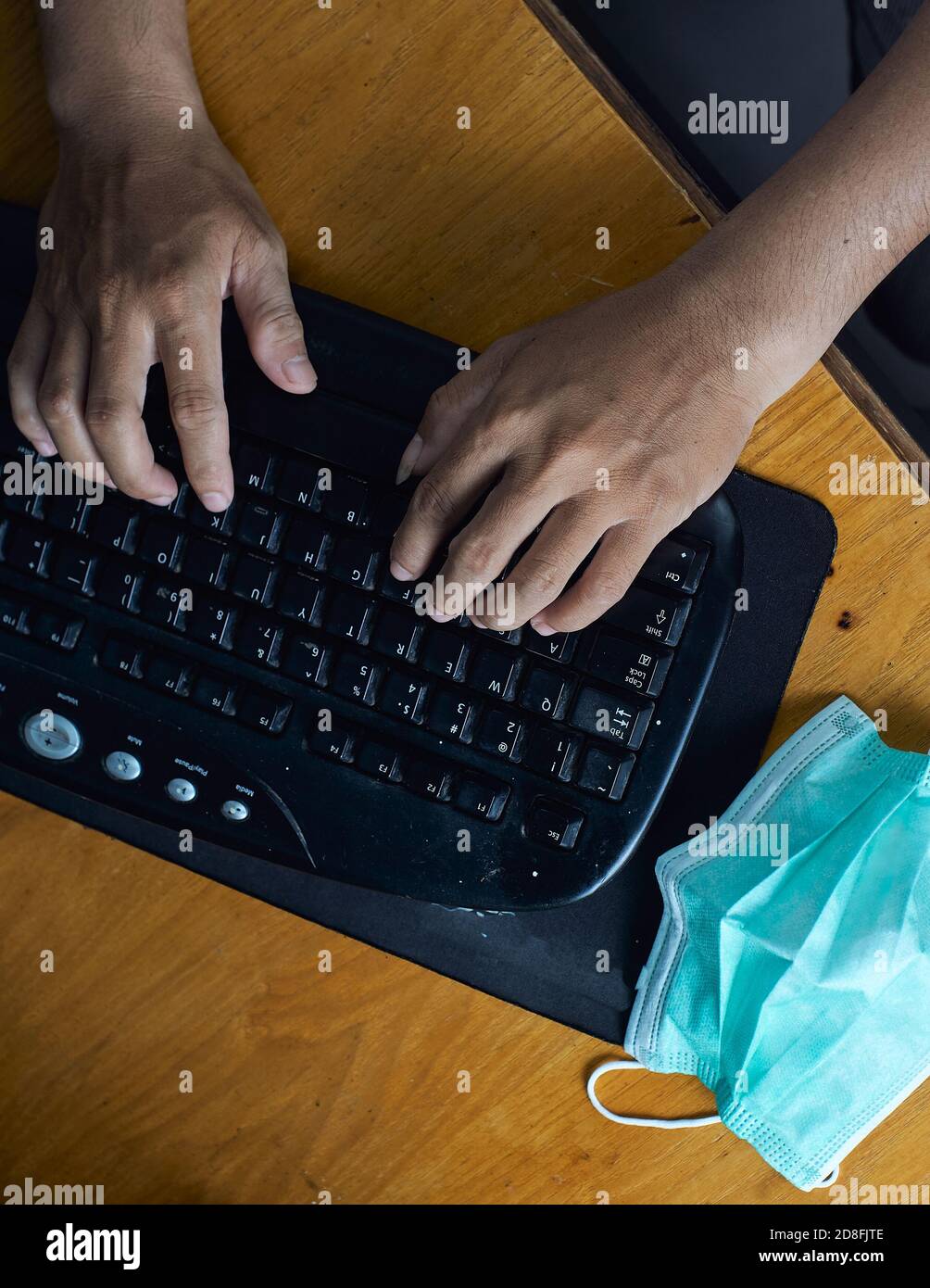 primo piano di mano uomo che digita sulla tastiera con maschera medica per la prevenzione durante la pandemia del virus corona. immagine vista dall'alto Foto Stock