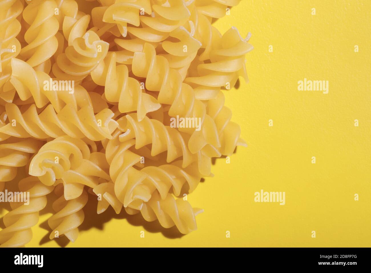 Pasta spirale su fondo grezzo asciutto su sfondo giallo brillante. Pasta di grano duro. Cucina tradizionale italiana. Cibo sfondo Foto Stock