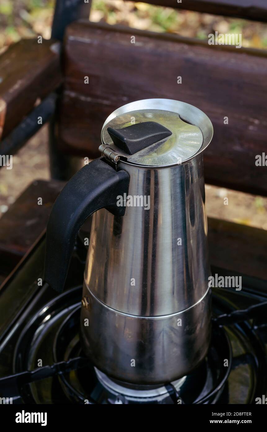 Macchina per caffè in metallo geyser e stufa a gas portatile su panca di  parcheggio. Processo di preparazione del caffè naturale durante un picnic o  un viaggio. Stile di vita Foto stock -