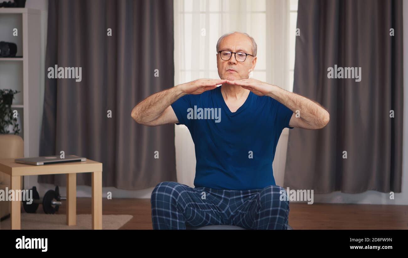 Uomo anziano che si esercita in soggiorno seduto sulla palla di stabilità. Anziano pensionato sano addestrando sport di salute a casa, esercitandosi attività di idoneità all'età anziana Foto Stock