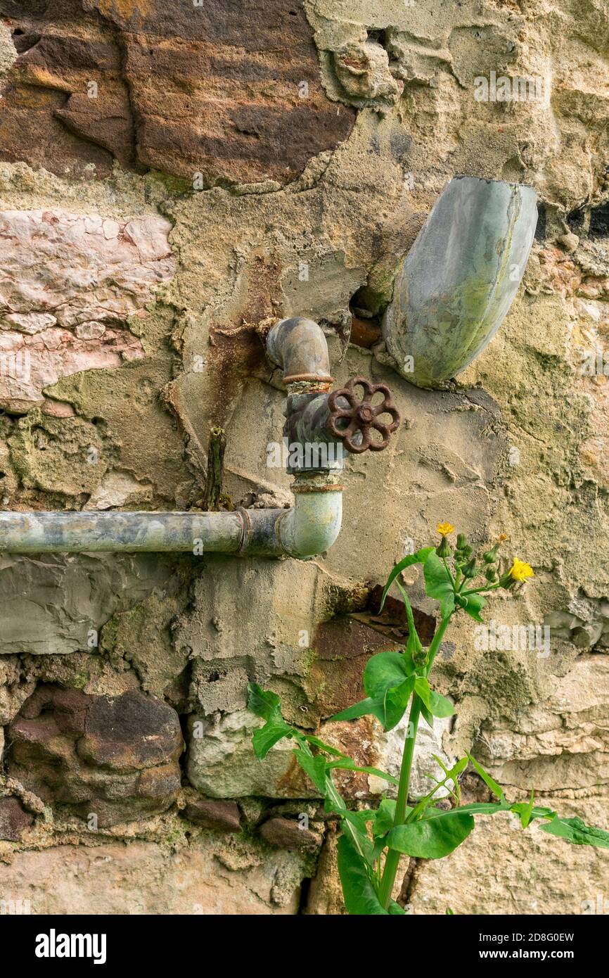 Vecchio misuratore di acqua arrugginita sporca e valvola arrugginita con tubi. Un sistema abbandonato per misurare la quantità di acqua consumata in una casa distrutta e in un'erba Foto Stock