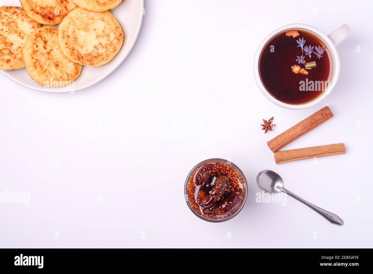 Frittelle di formaggio cottage con marmellata di fichi e tè nero aromatico caldo, umore della colazione di Natale con anice e cannella su sfondo bianco, vista dall'alto Foto Stock