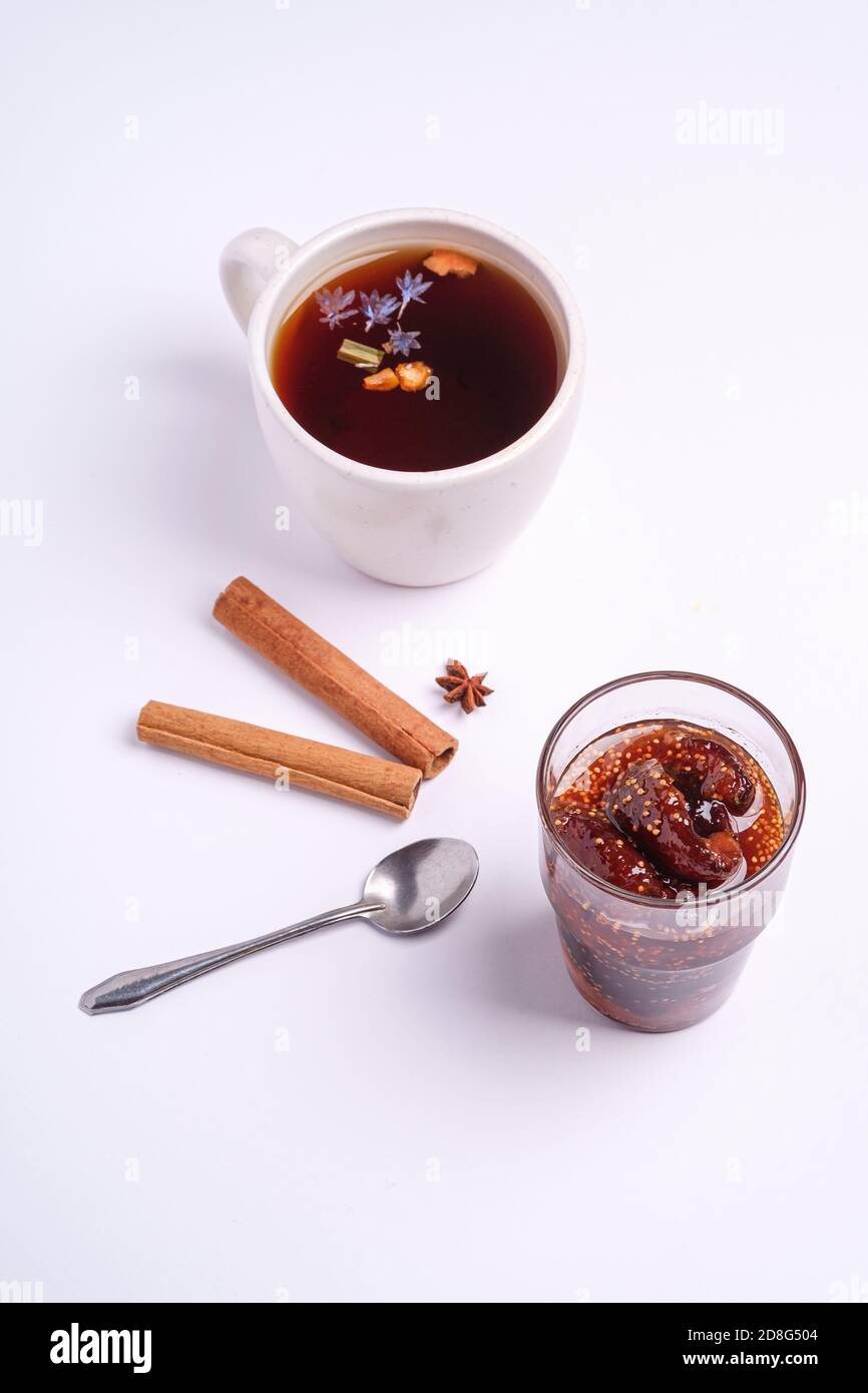 Tè nero aromatico caldo vicino alla marmellata di fichi, umore della colazione di Natale con anice e cannella su sfondo bianco, vista angolare Foto Stock