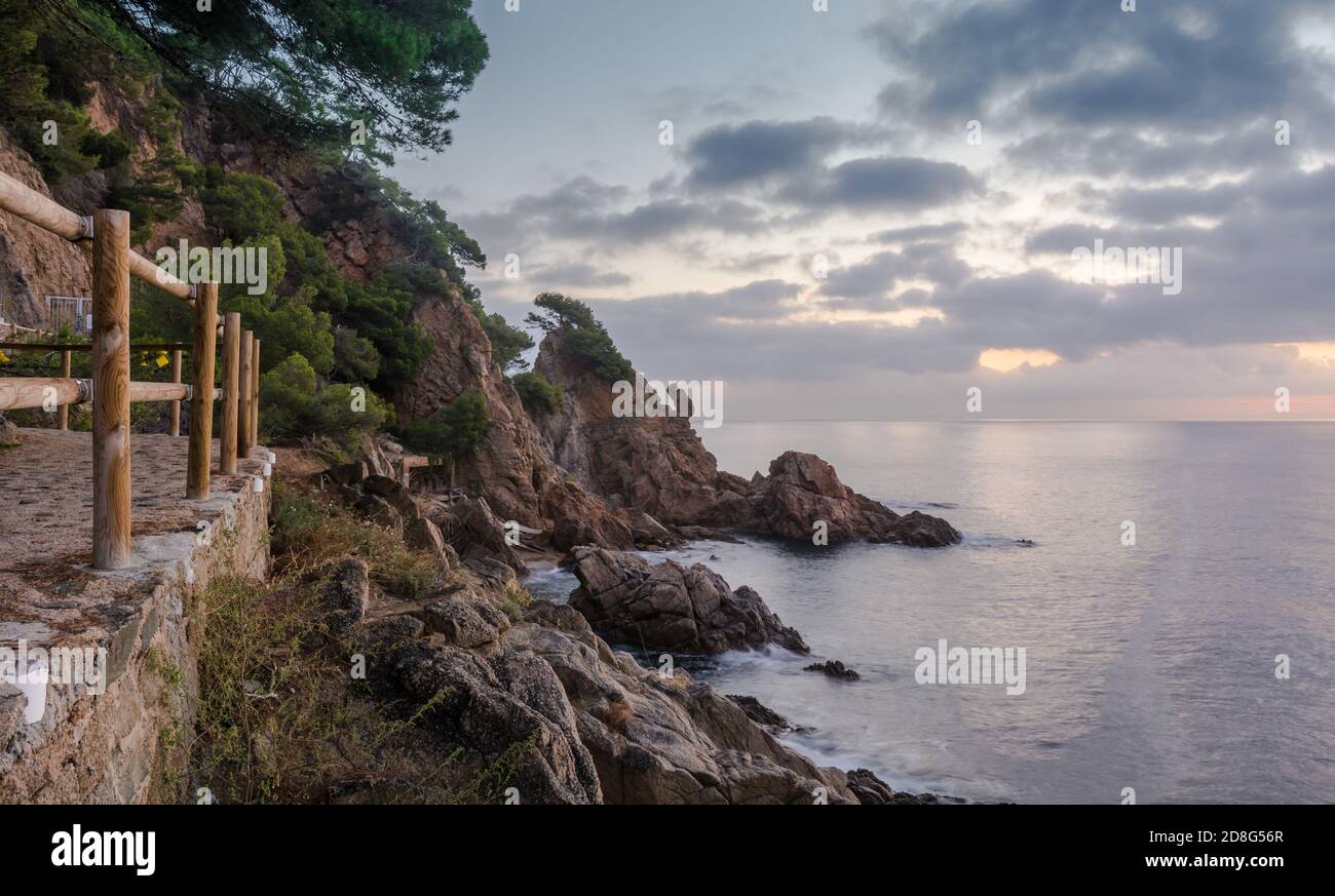 Alba sulla spiaggia di Blanes nel cuore della Costa Brava in Spagna. Paesaggio costiero con rocce e montagne di fronte al mare. Foto Stock