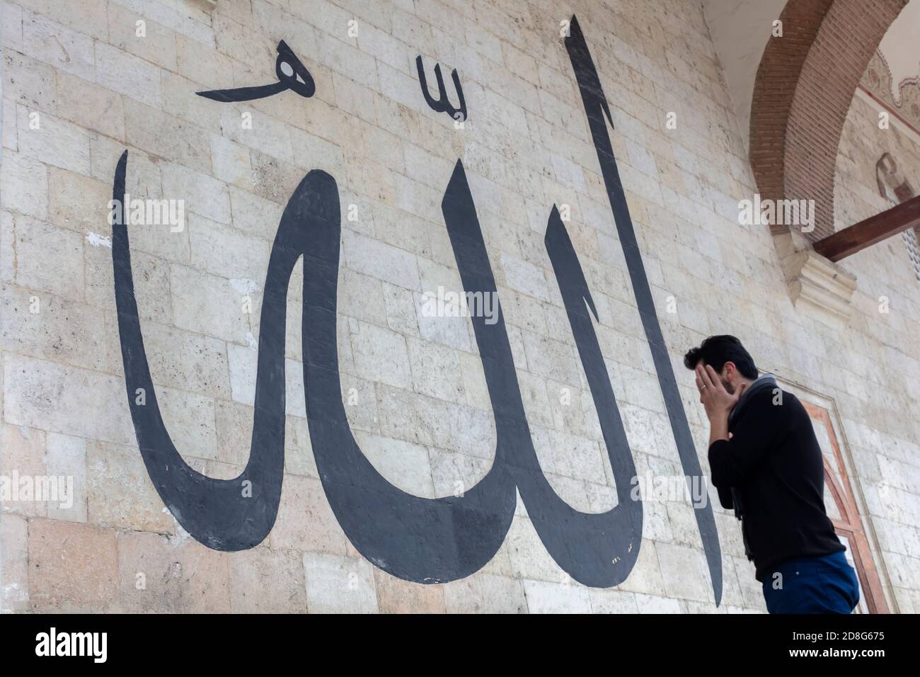 Giovane uomo che staring alla Calligraphy araba che significa 'Allah-Dio in Islam' sul Muro della vecchia Moschea di Edirne Foto Stock