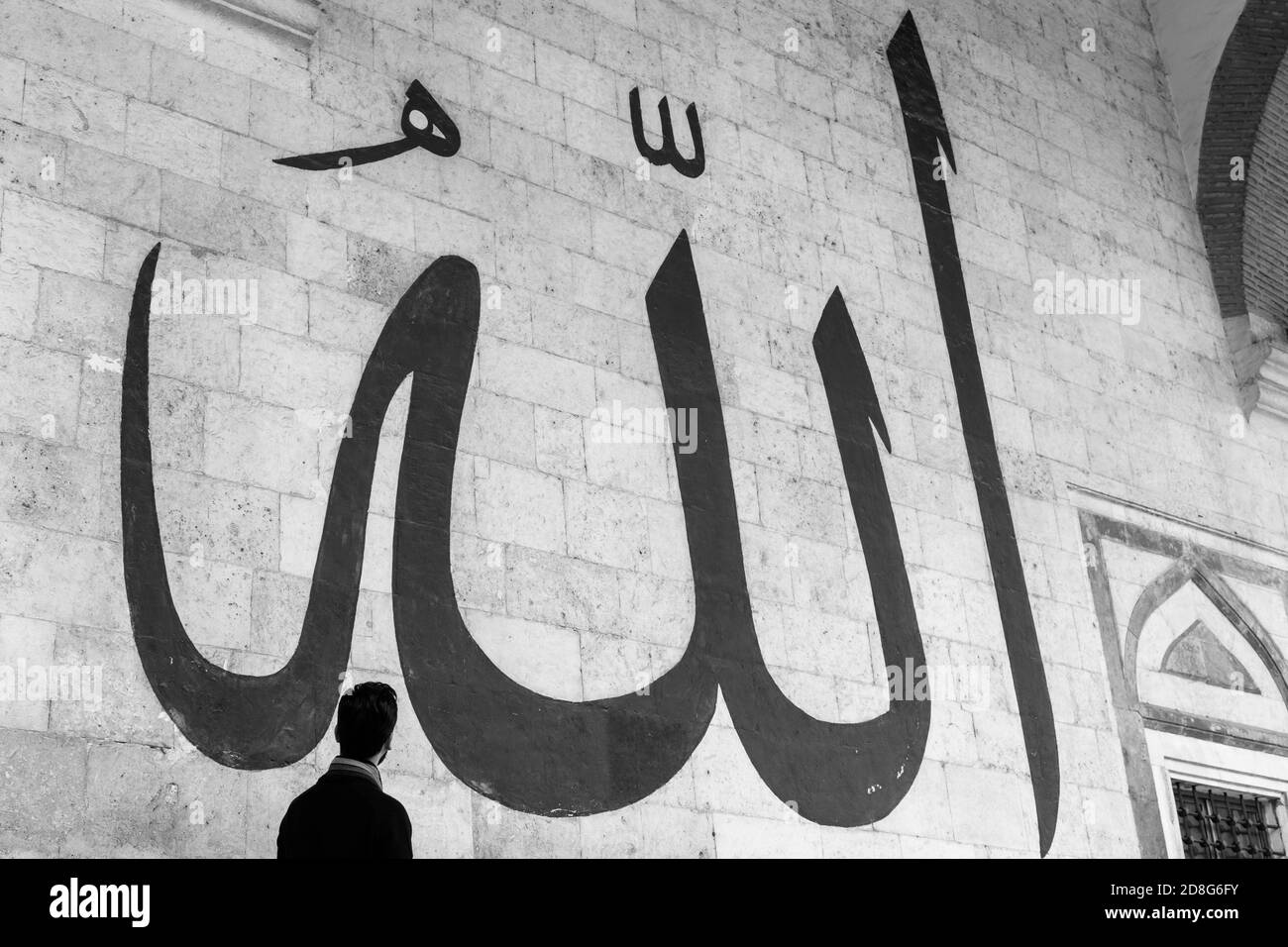 Giovane uomo che staring alla Calligraphy araba che significa 'Allah-Dio in Islam' sul Muro della vecchia Moschea di Edirne Foto Stock