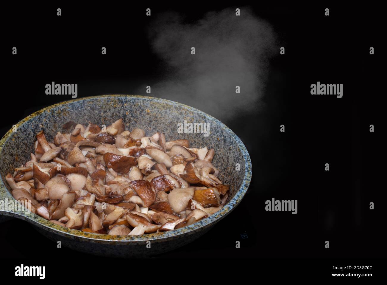 Primo piano di funghi fritti o stufati in una padella, il vapore sale da funghi caldi, isolati su fondo nero Foto Stock