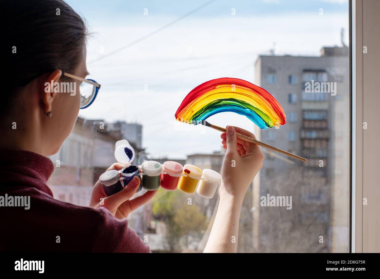 La ragazza disegna un arcobaleno, tiene le vernici in mano, termina la quarantena, il supporto dei medici, soggiorno a casa, flash MOB Foto Stock