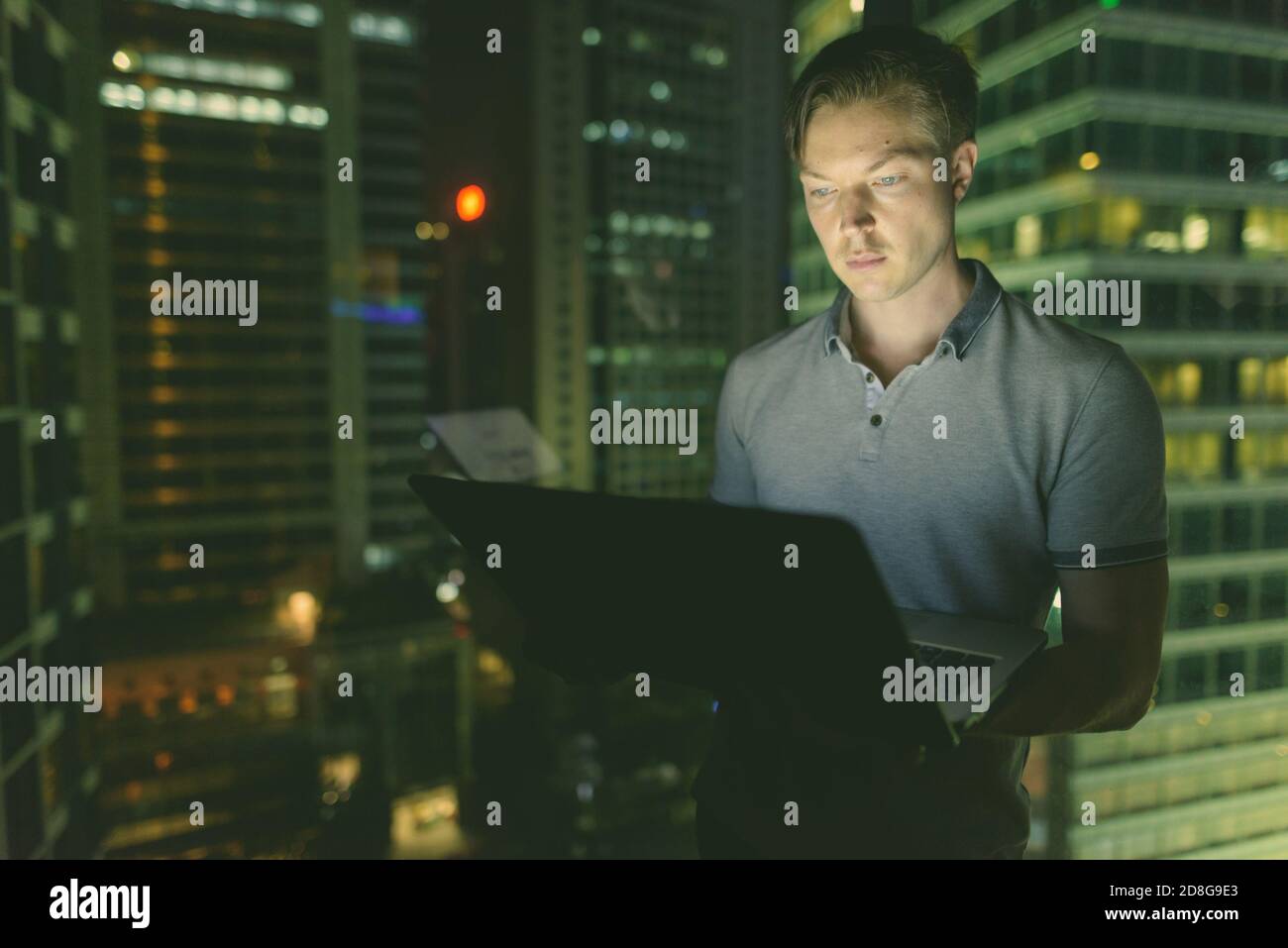 Giovane bell'uomo che usa il laptop contro la finestra di vetro con vista della città di notte Foto Stock