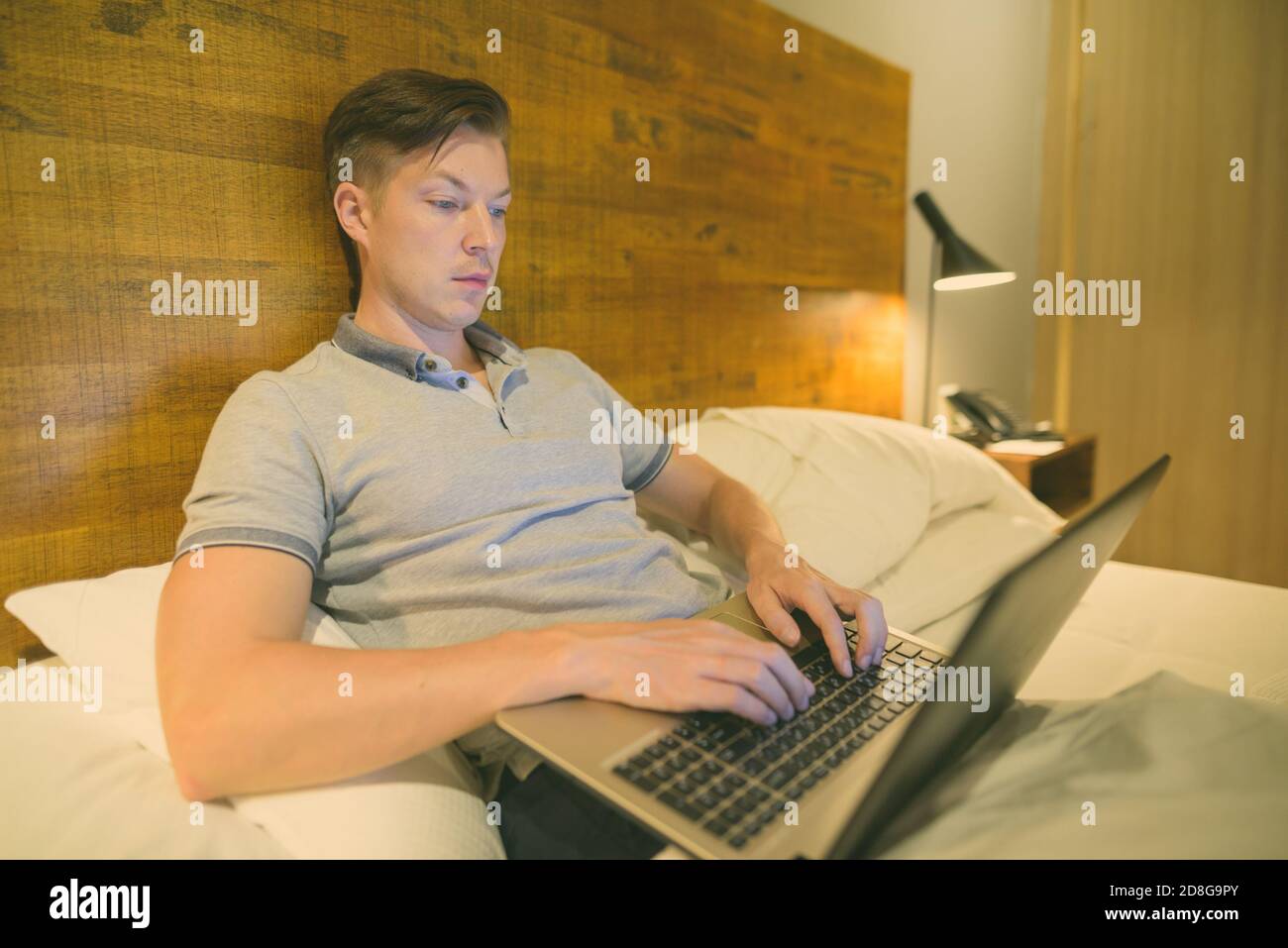 Giovane bell'uomo che usa il computer portatile mentre è comodo in camera da letto Foto Stock