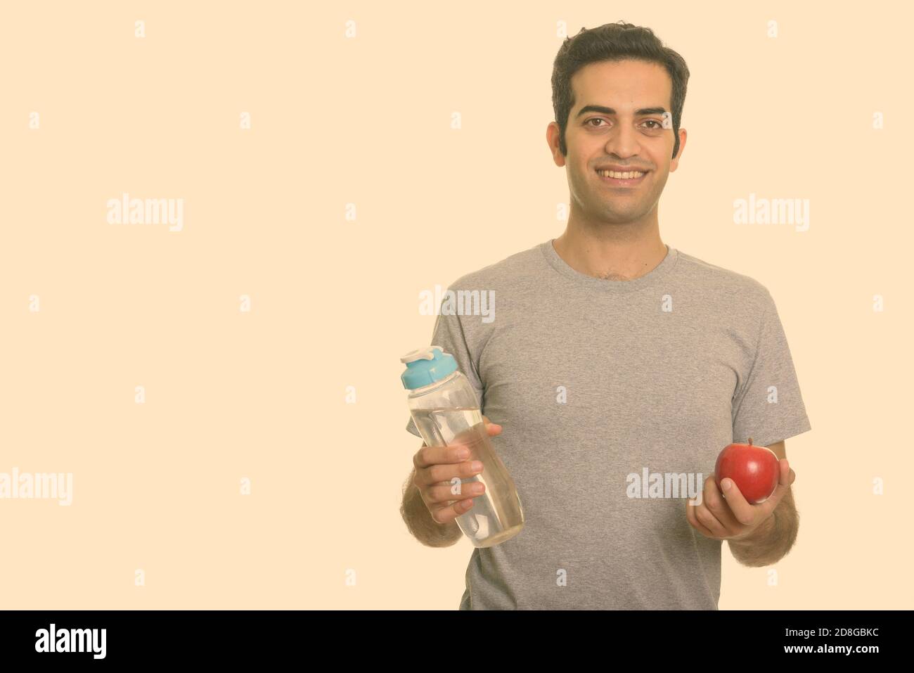 Giovani felici uomo persiano tenendo la bottiglia di acqua e mela rossa pronto per la palestra Foto Stock