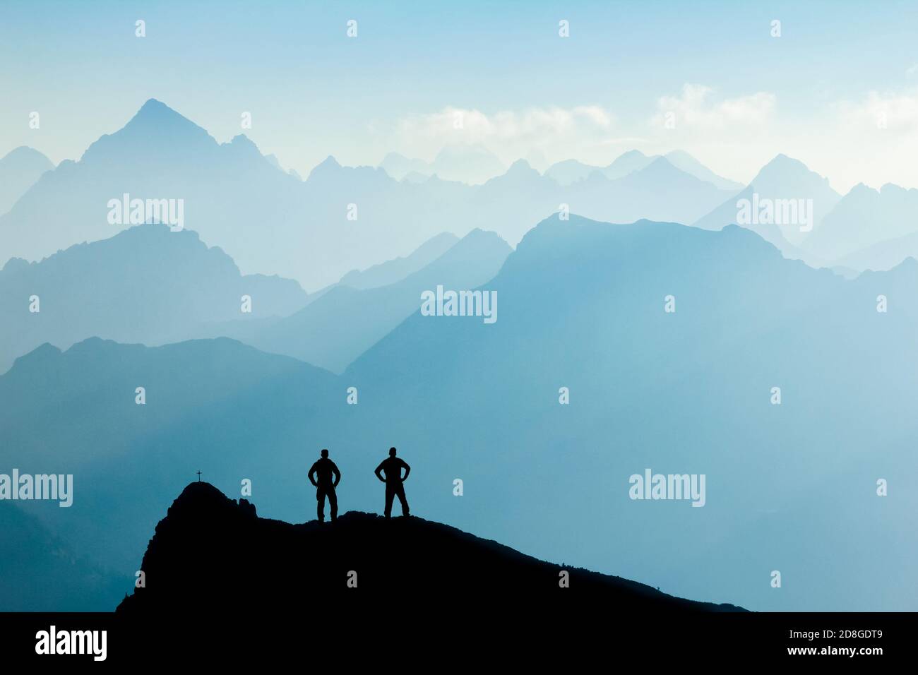 Due uomini che raggiungono la vetta dopo l'arrampicata e le escursioni godendo la libertà e guardando verso le montagne sagome panorama durante l'alba. Foto Stock