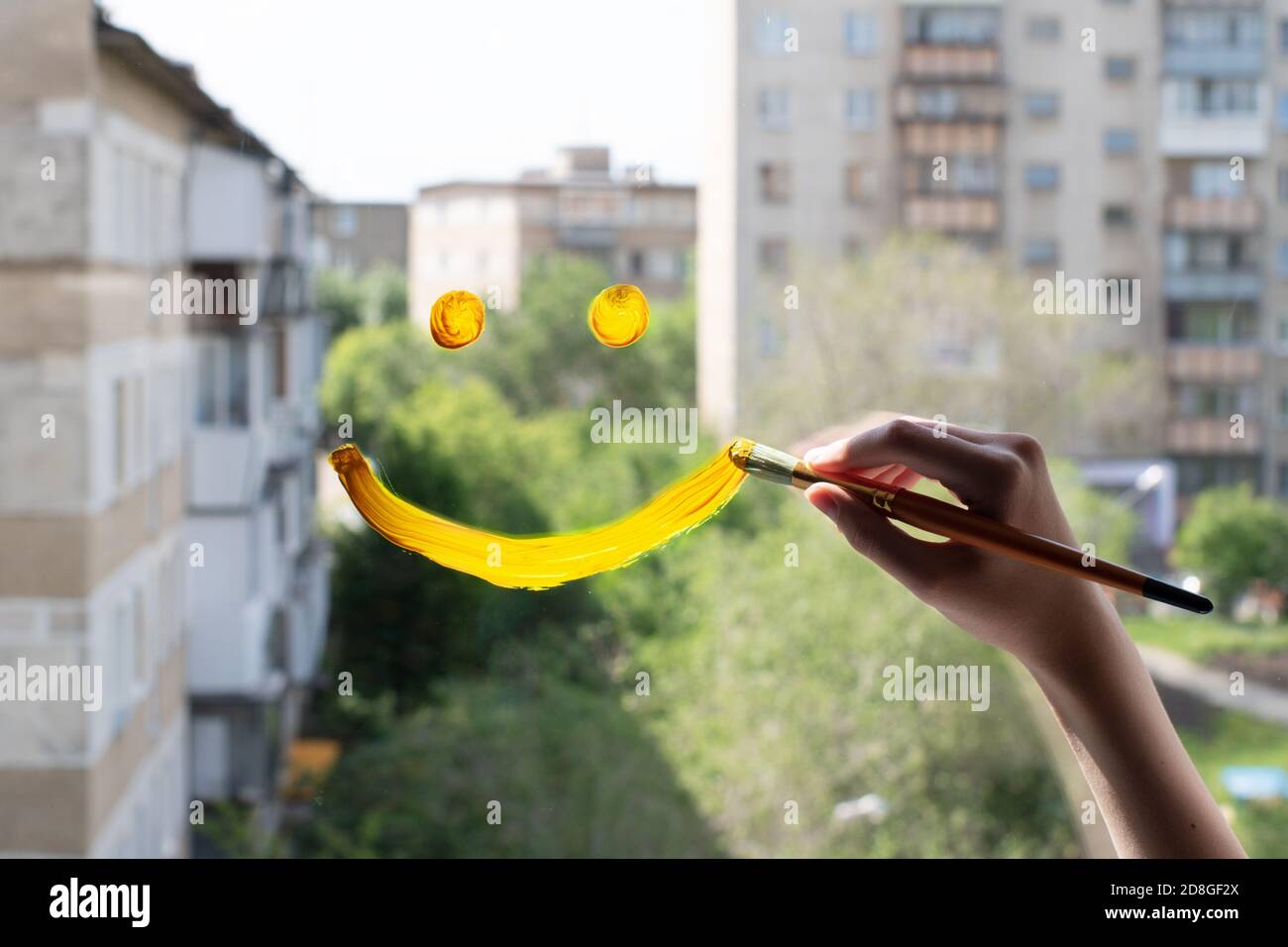 La mano femminile in primo piano disegna un sorriso giallo sul vetro contro un cielo blu. Il concetto di gioia per un nuovo giorno, buona fortuna Foto Stock