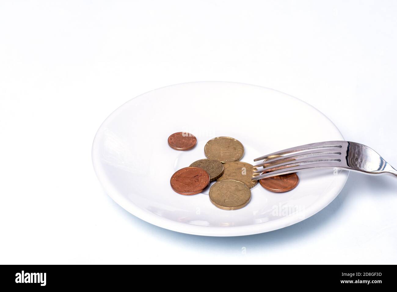 Monete Euro cent su un piatto bianco con una forchetta su sfondo bianco, primo piano, spazio per la copia. Concetto di crisi dell'economia alimentare Foto Stock
