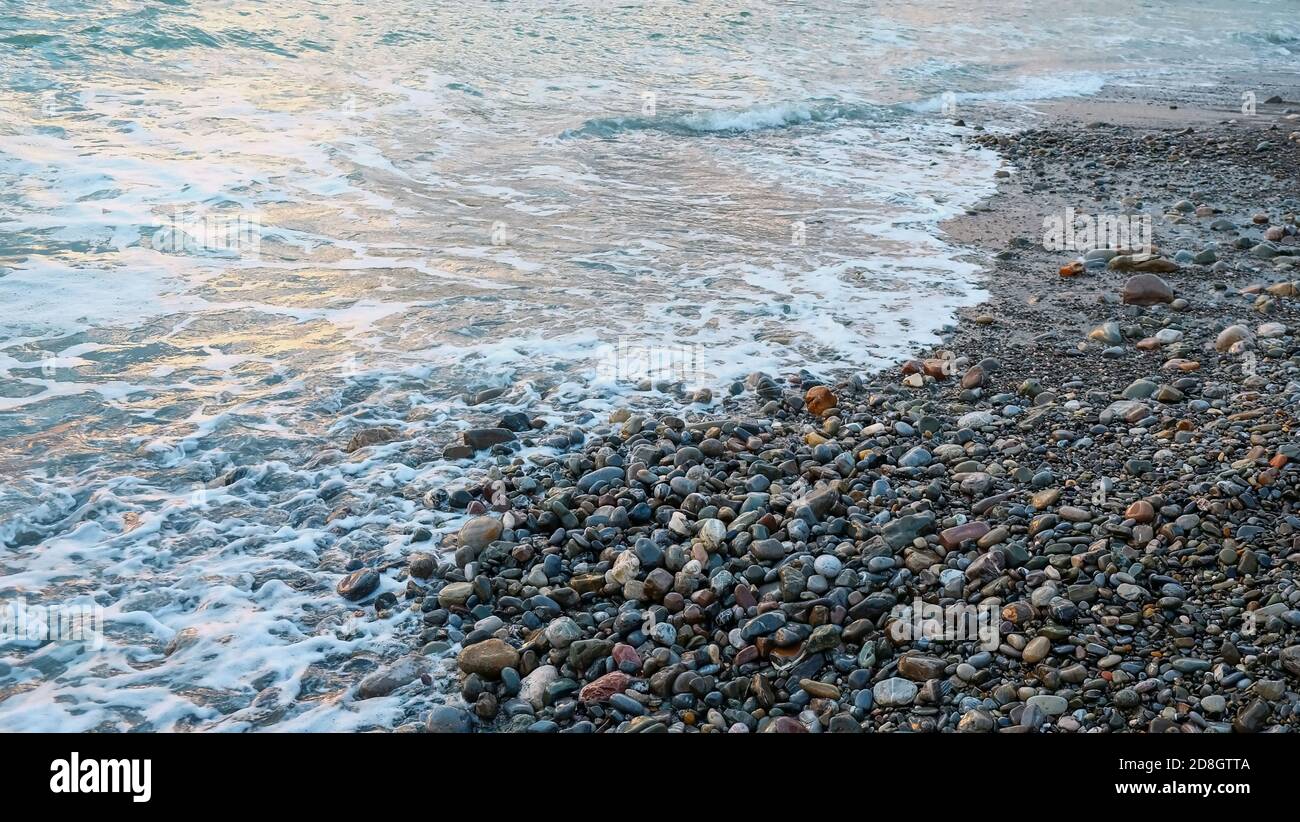 Onde fredde con marea ascendente con schiuma di mare e ciottoli bagnati nel clima invernale nuvoloso cattivo fickle. Cambiamento di stagione, tema di riscaldamento globale, turismo invernale. Foto Stock