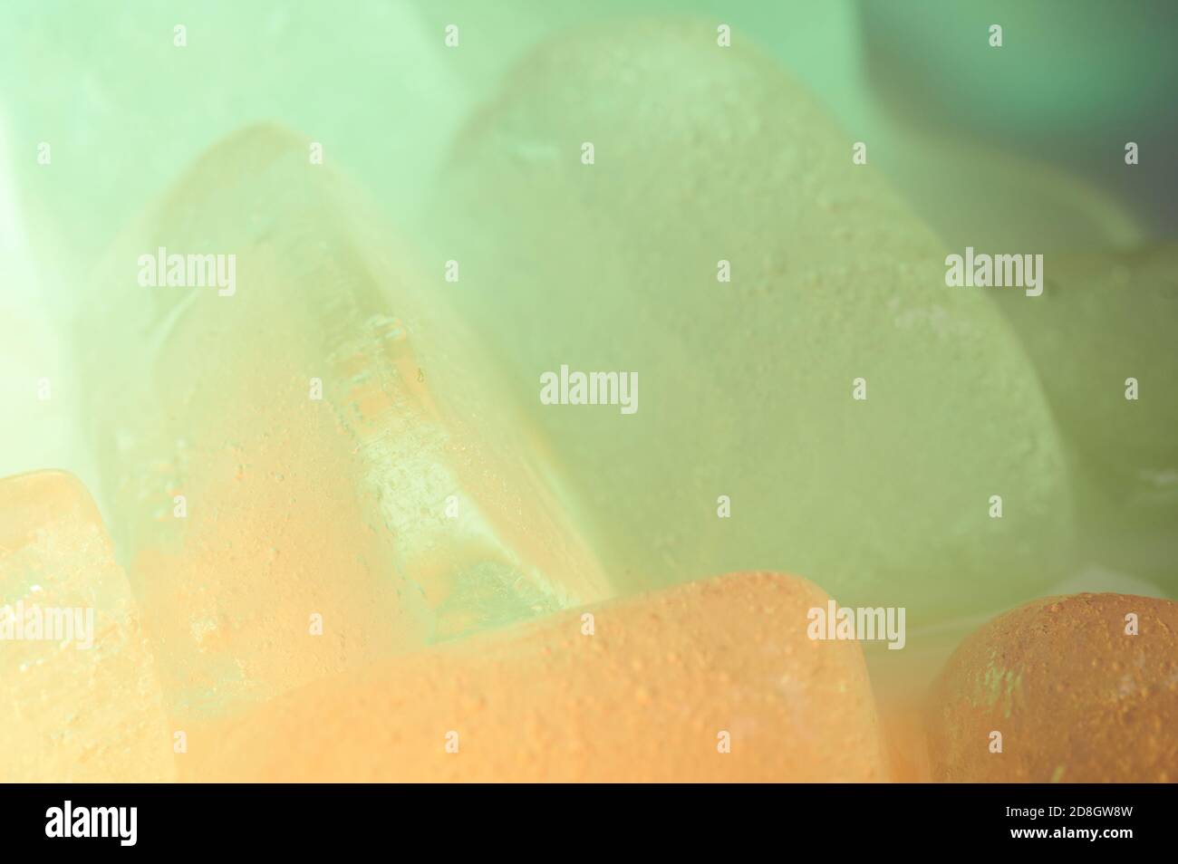 Sfondo colorato e gelido. Cubetti di ghiaccio di colore verde e arancione Foto Stock