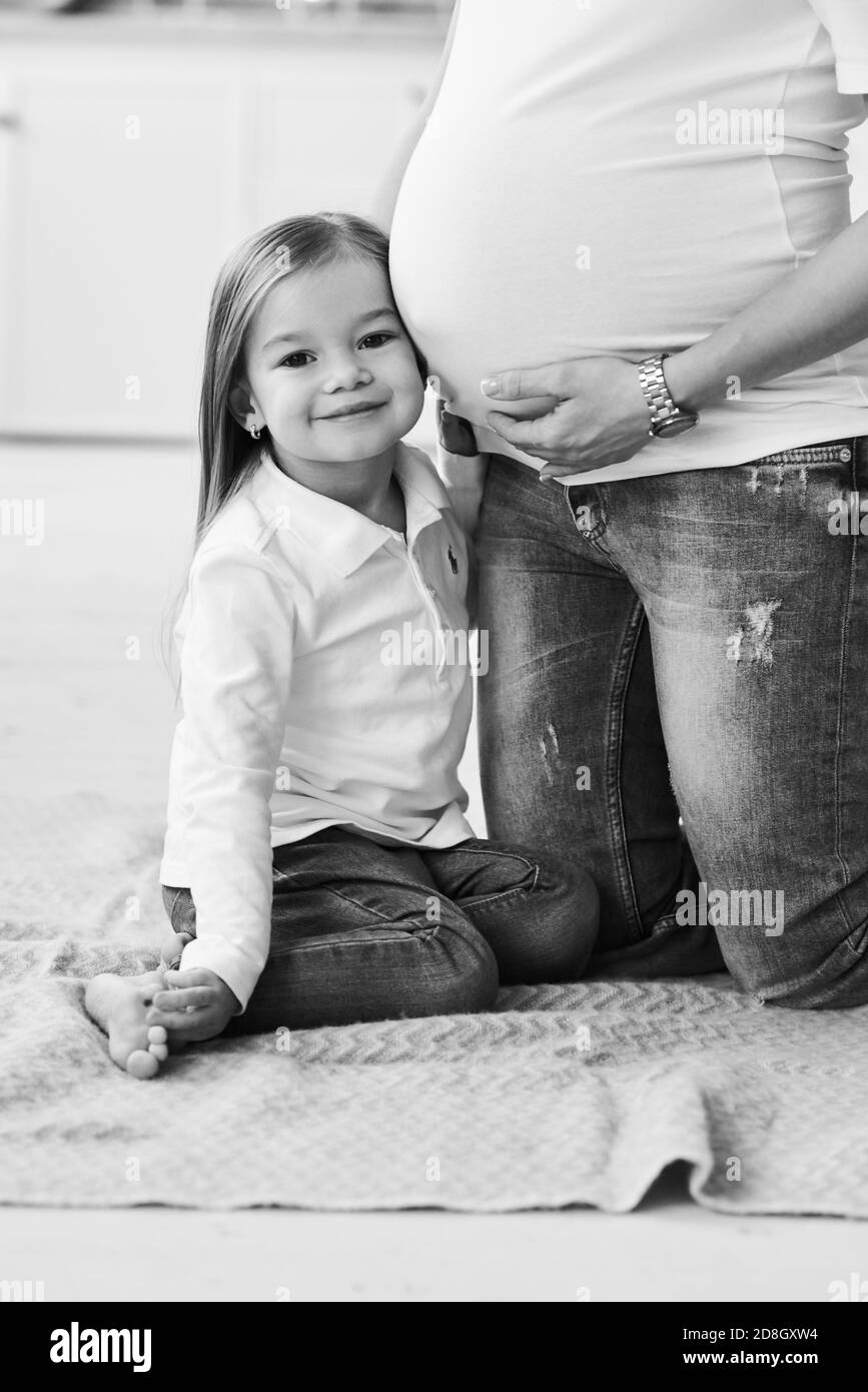 Un ritratto di una piccola figlia con la madre incinta in cucina su uno sfondo di mattoni con un sfocato luci Foto Stock