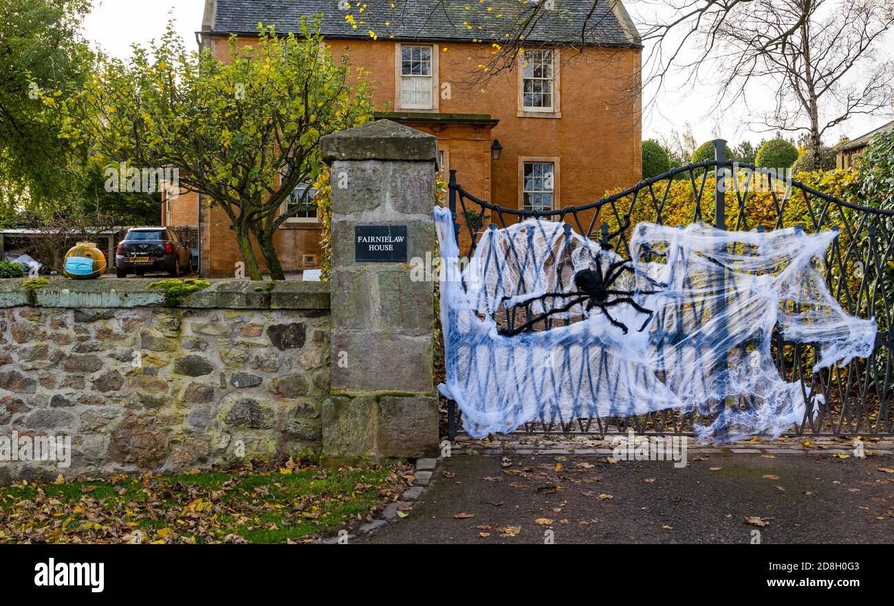 East Lothian, Scozia, Regno Unito, 30 ottobre 2020. Decorazioni di Halloween: Una casa in Athelstaneford entra nello spirito di Halloween decorando una porta con un grande web di ragno e ragno falso così come le zucche su una parete, uno che indossa una maschera facciale Foto Stock
