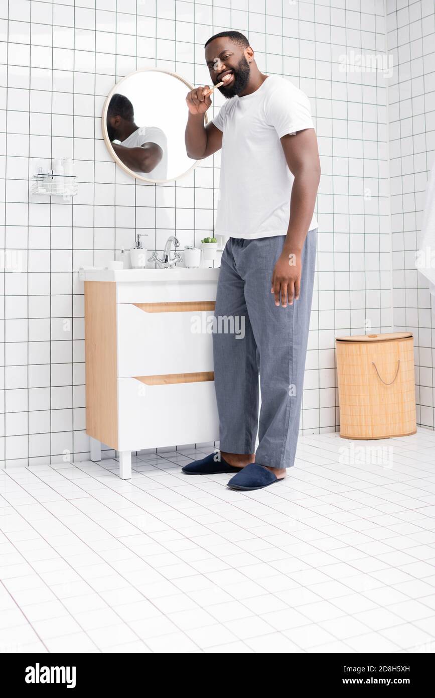 tutta la lunghezza di un uomo afro-americano spazzolando i denti in bagno Foto Stock