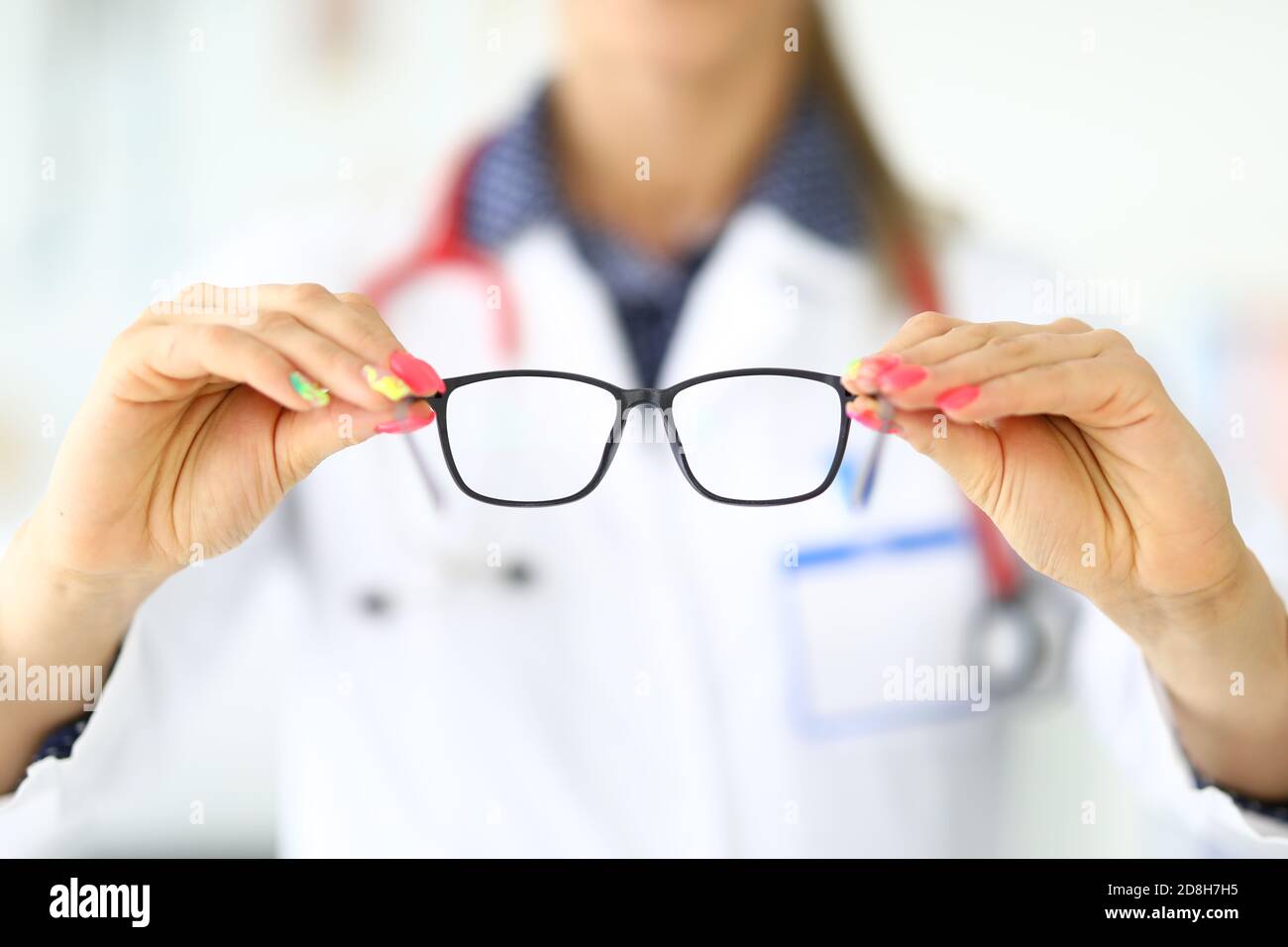 L'oftalmologo con stetoscopio intorno al collo tiene gli occhiali per la visione in primo piano della clinica Foto Stock