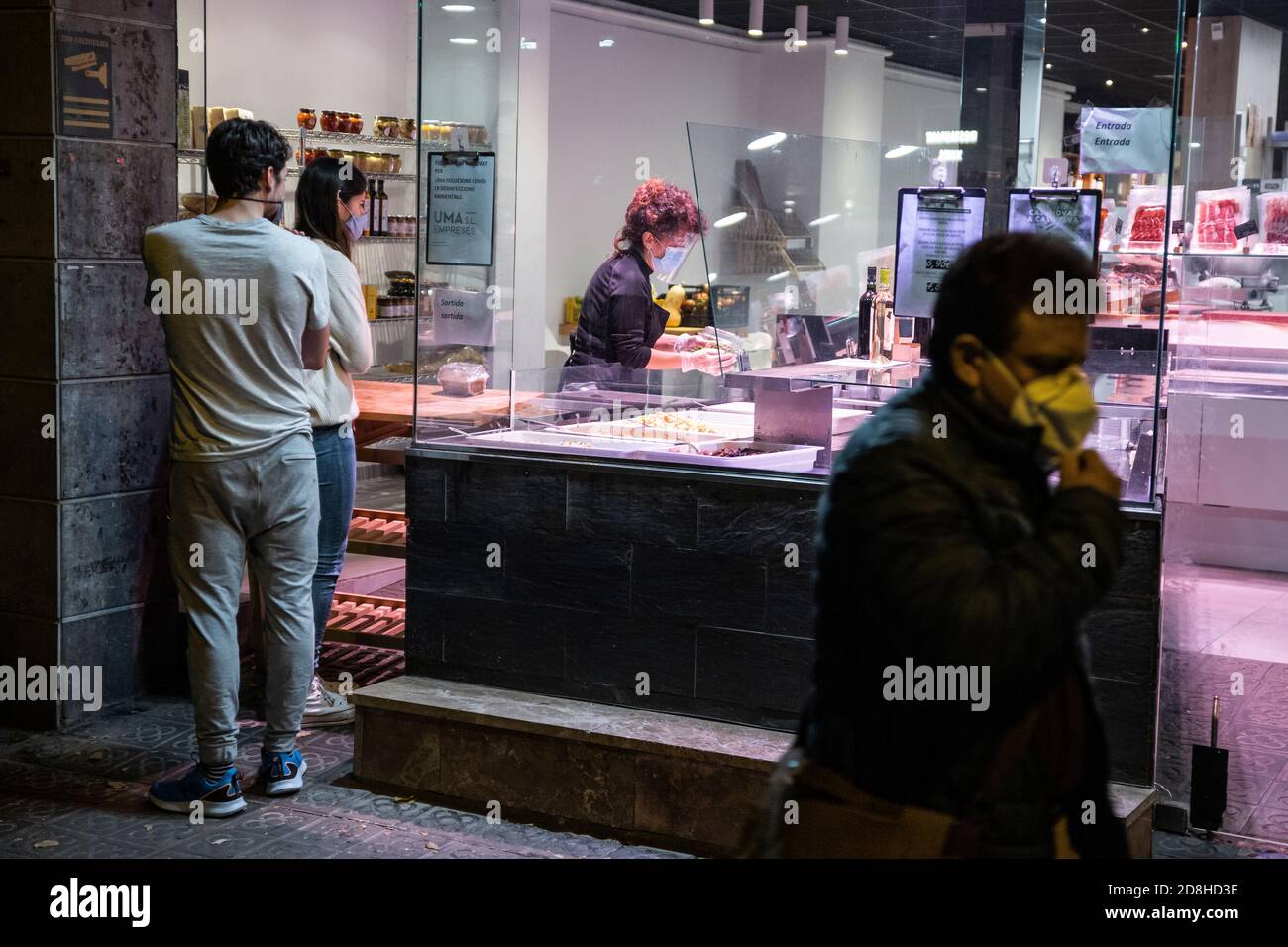 Barcellona, Spagna. 2020.10.29. Un assistente in un negozio di alimentari da take-out serve due clienti al di fuori degli orari di chiusura per i negozi secondo il coprifuoco. Foto Stock