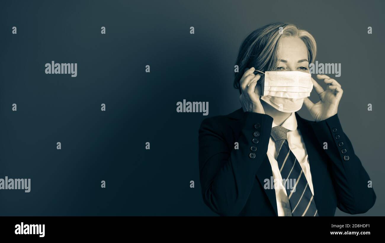 La donna di affari pensiva raddrizza la sua maschera di faccia in piedi su sfondo grigio con lo spazio di copia a sinistra. Immagine in bianco e nero con toni Foto Stock