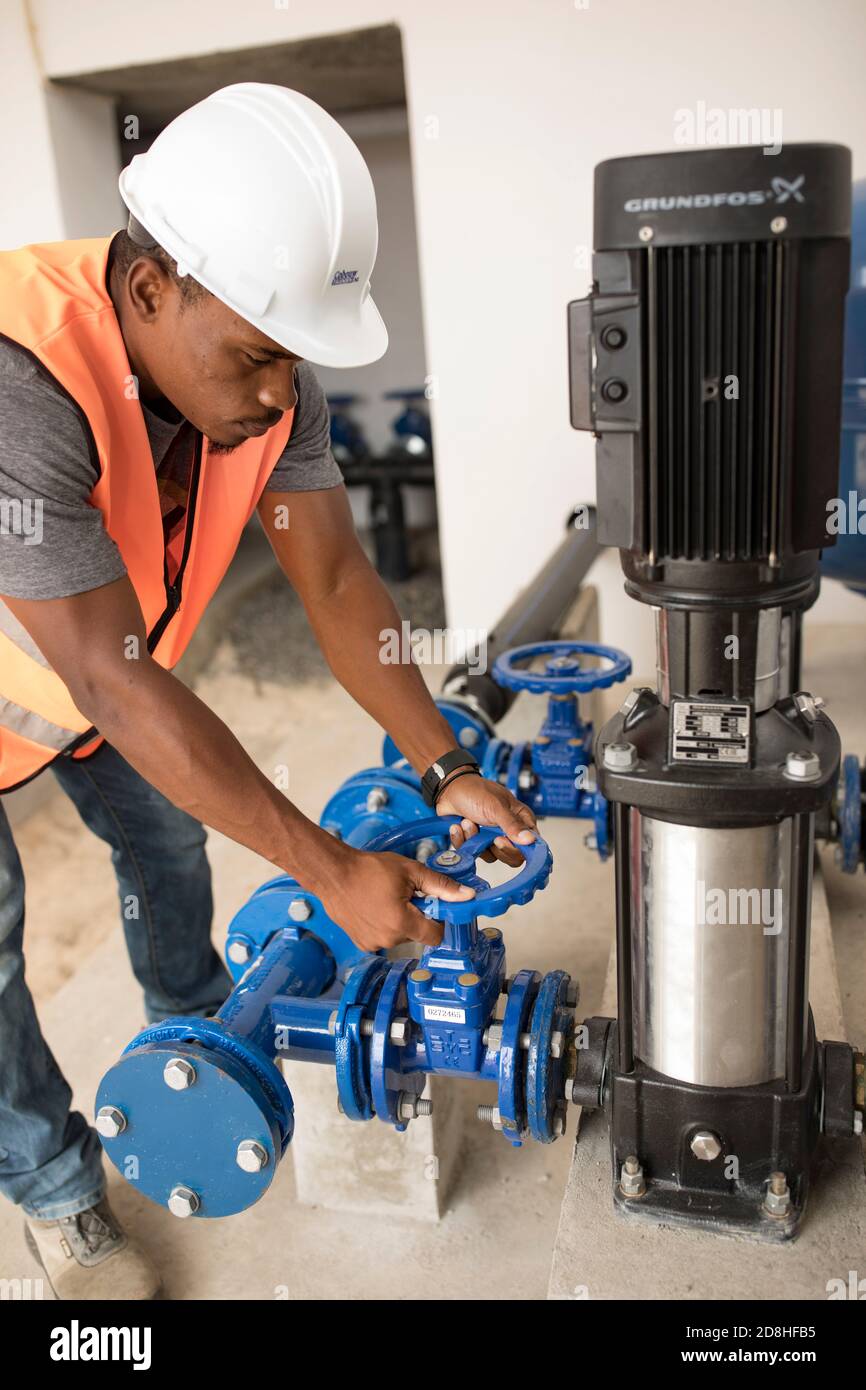 Un lavoratore maschile professionista gestisce una nuova valvola per attrezzature presso un serbatoio dell'acqua e una stazione di pompaggio sull'isola di Maio, Cabo Verde. Foto Stock