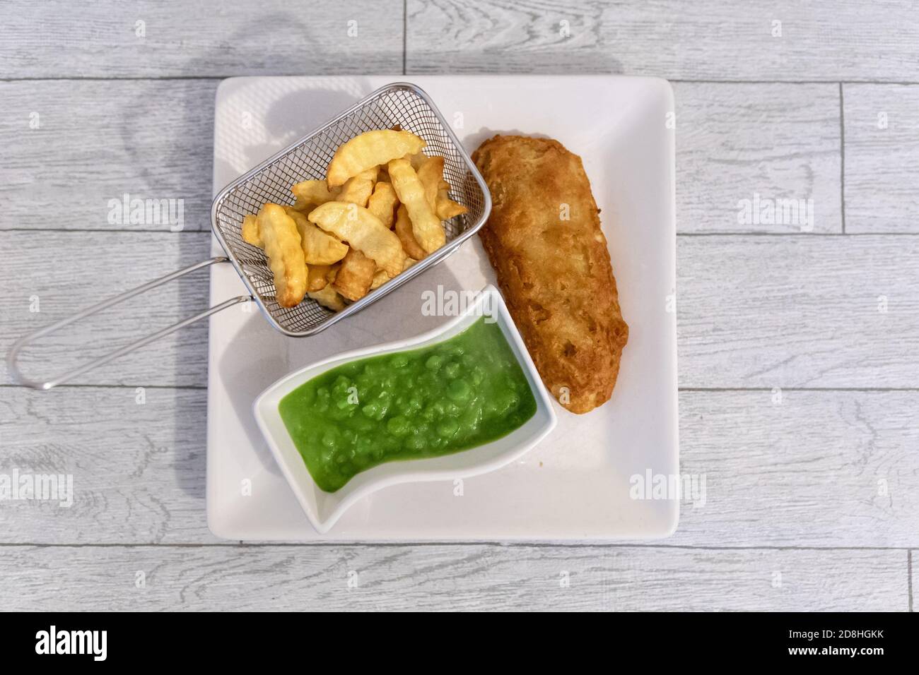 Cena a base di pesce, patatine e piselli moschi servita su un piatto quadrato visto dall'alto. Una cena tradizionale inglese spesso il venerdì. Foto Stock