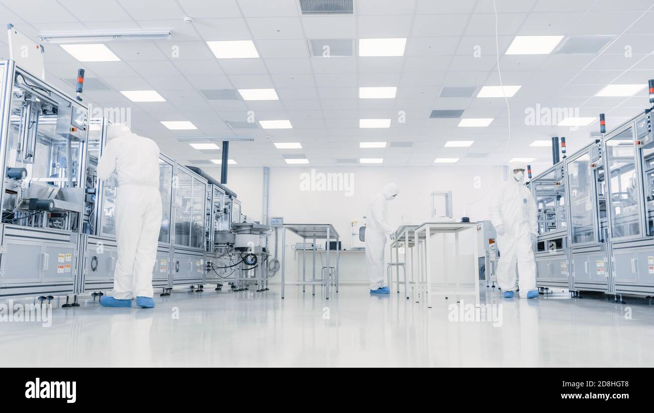 Team di ricercatori in tute sterili che lavorano con computer, microscopi e macchinari industriali moderni in laboratorio. Prodotto Foto Stock