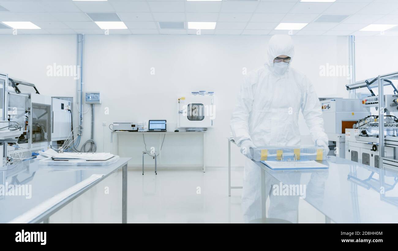 Scienziato in tuta protettiva che lavora con Case di prodotto finito attraverso il laboratorio. Lavoratori nello stabilimento con macchinari industriali moderni Foto Stock