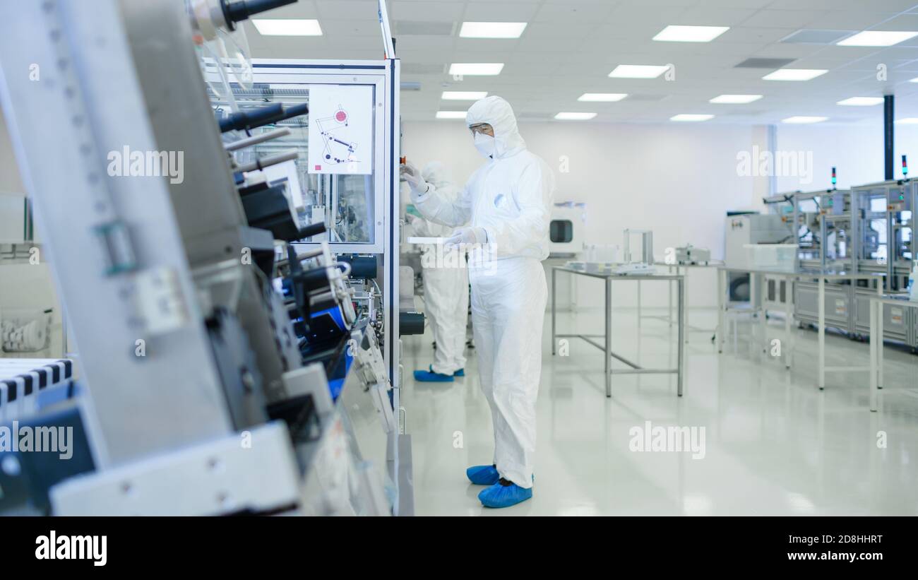 Laboratorio di produzione sterile ad alta precisione in cui gli scienziati della tuta protettiva accinggono alla lavorazione della macchina, utilizzano computer e microscopi Foto Stock