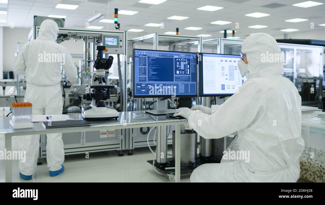 Shot di scienziati in tute sterili che lavorano con i computer, analisi dei dati forma macchinari industriali moderni in laboratorio. Produzione di prodotti Foto Stock