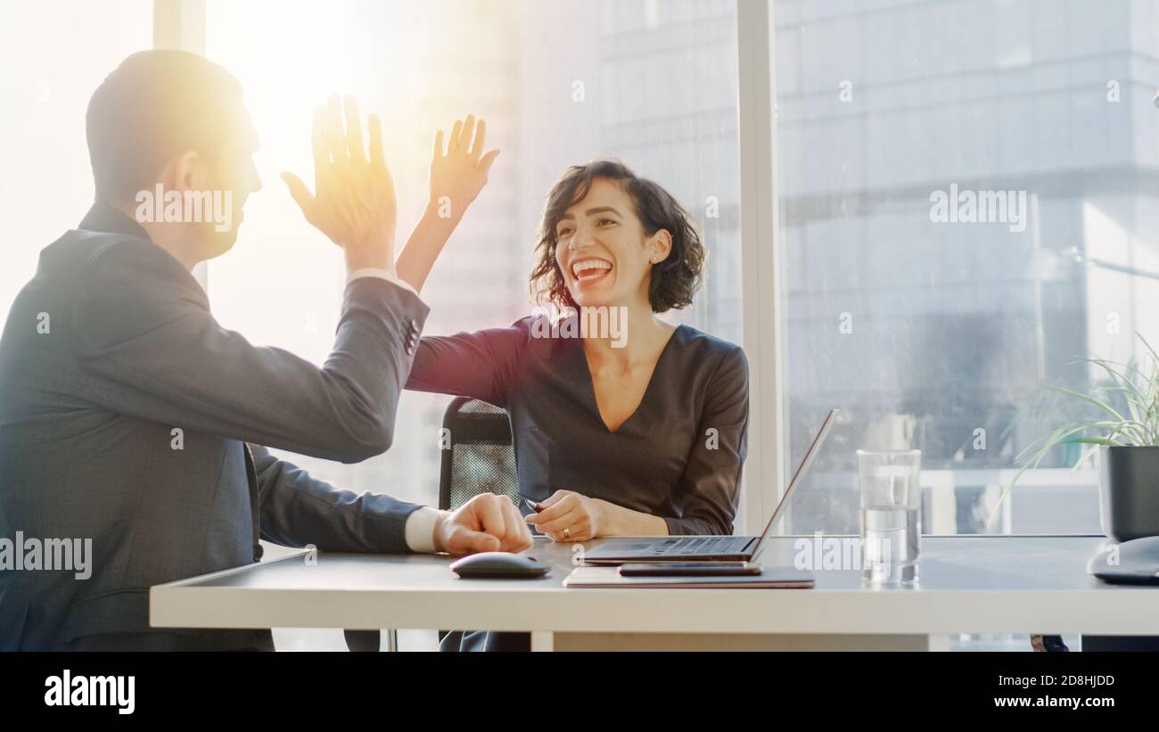 Donna Top Manager e uomo d'affari seduto alla scrivania e fare High Five dopo aver trovato una soluzione di successo al problema. Bella gente dentro Foto Stock