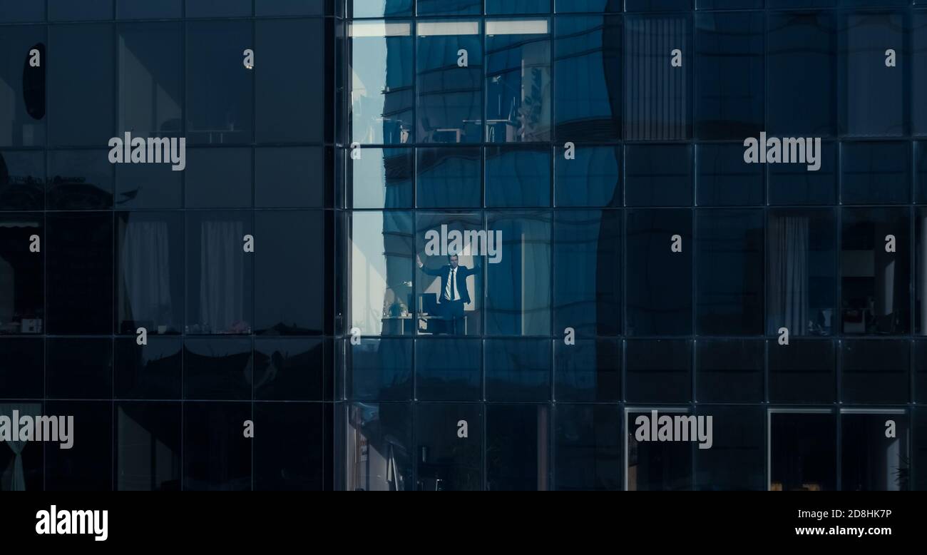 Fotografia aerea: Dall'esterno all'edificio degli uffici con un uomo d'affari che lavora e che guarda fuori dalla finestra. Foto del Financial Business District Foto Stock