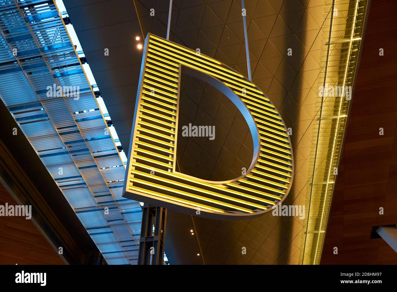 Una grande D illuminata di giallo segna un atrio all'aeroporto internazionale di Hamad a Doha, Qatar. Foto Stock