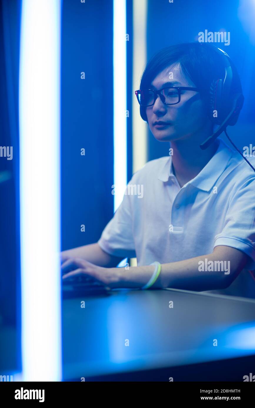 Videogamer professionista che gioca Online Video Game sul suo Personal computer. Sta parlando con il suo team tramite la cuffia. Stanza illuminata da luci Neon in retro Foto Stock