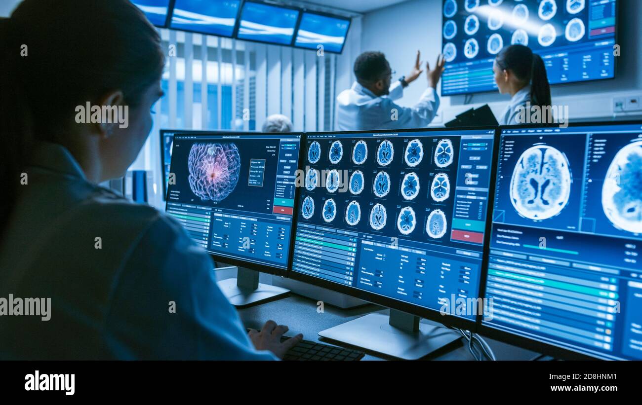 Over the Shoulder Shot of Female Medical Scientist lavorare con immagini Brain Scan su un personal computer in laboratorio. Centro di ricerca neurologica Foto Stock