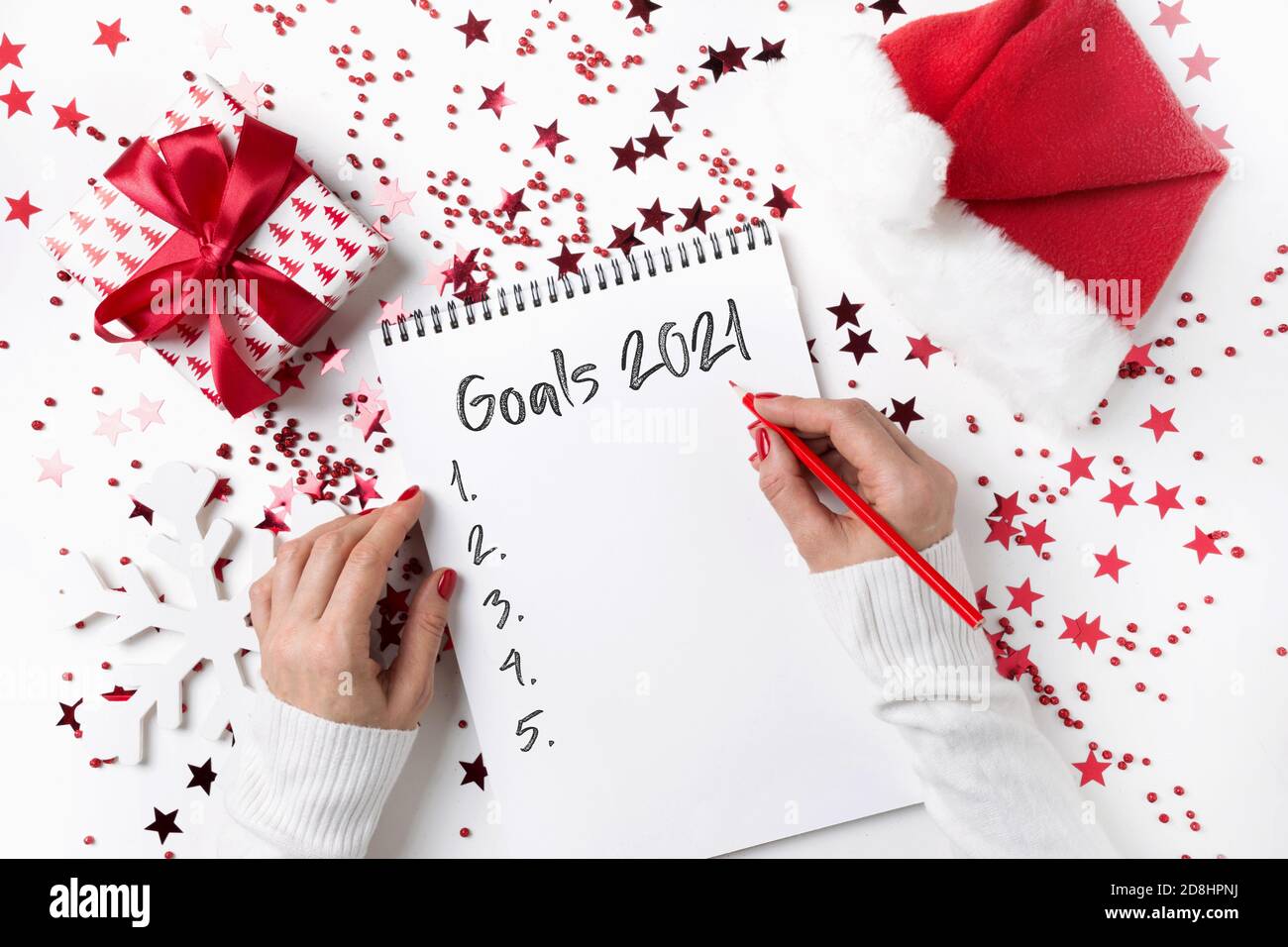 Lista di controllo di Natale con nuovi desideri e sogni intorno alle decorazioni rosse di festa. Donna che scrive wishlist o fare lista per il nuovo 2021 anno. Vista dall'alto. Foto Stock