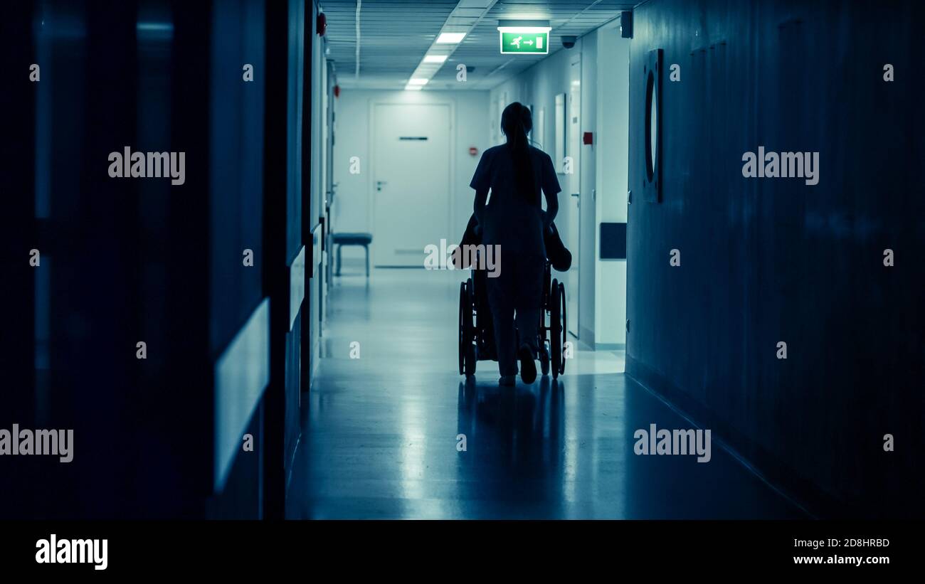 Silhouette del paziente in movimento infermiere femminile nella sedia a rotelle alla fine del corridoio ospedaliero. Esecuzione delle procedure. Luminoso Ospedale moderno con Foto Stock