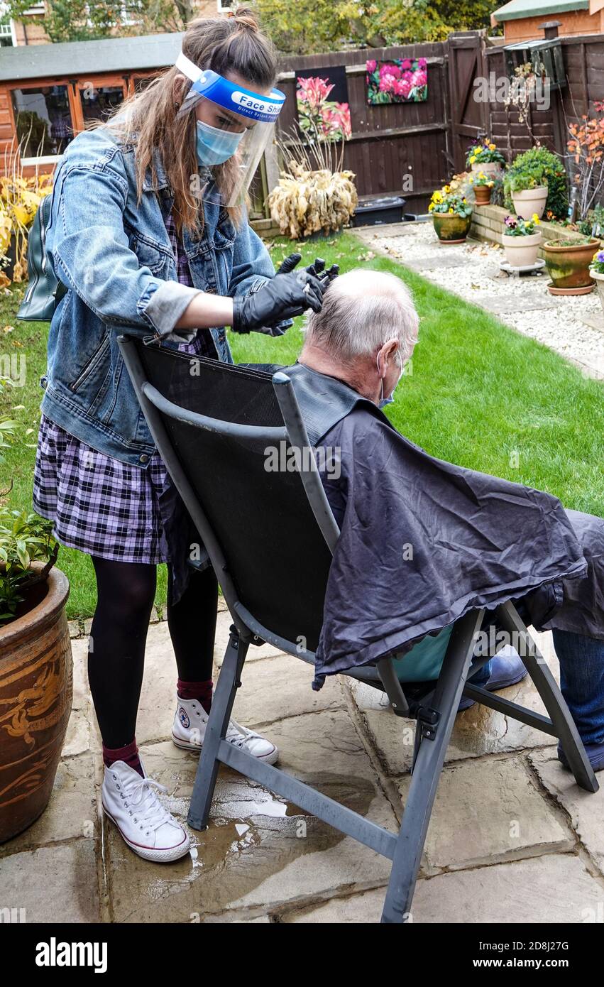 Un parrucchiere mobile freelance si occupa di uno dei capelli del suo cliente nel giardino posteriore durante il covid 19 o pandemia, covid 19 epidemia in Inghilterra. Foto Stock