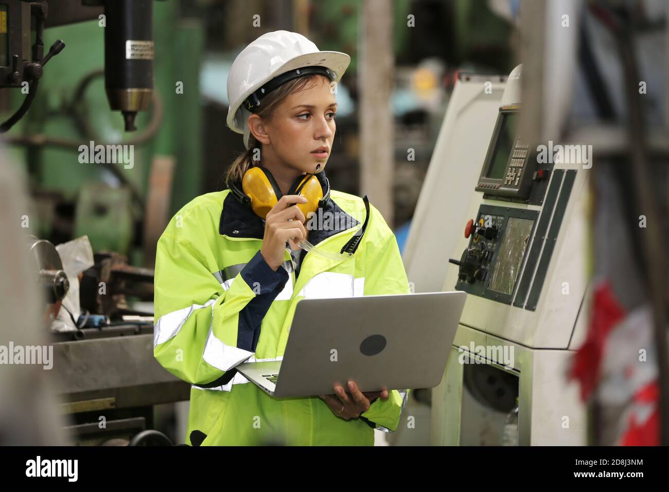 Operatrice di tecnici in uniforme che lavora su un computer portatile con una macchina in produzione. Foto Stock