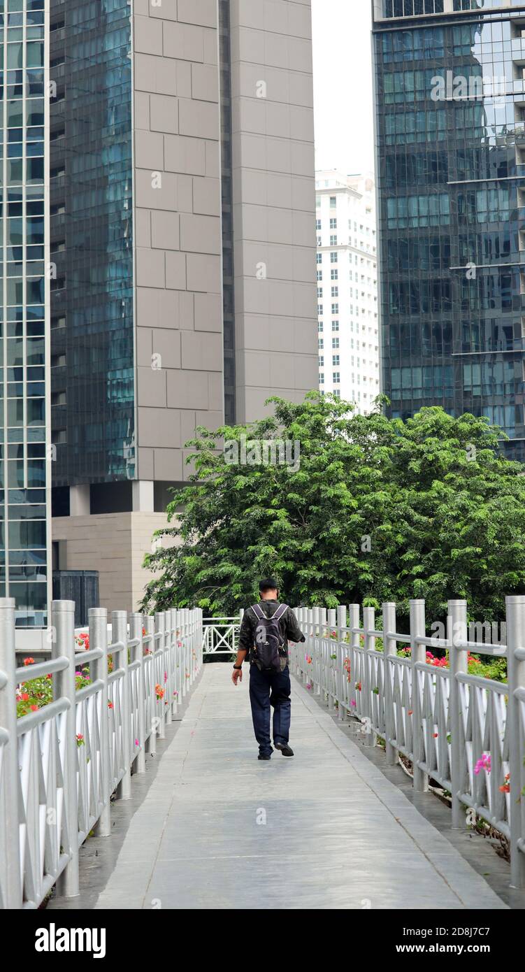 un uomo che attraversa un ponte pedonale senza tetto con un edificio d'ufficio sullo sfondo. seguire le indicazioni stradali Foto Stock