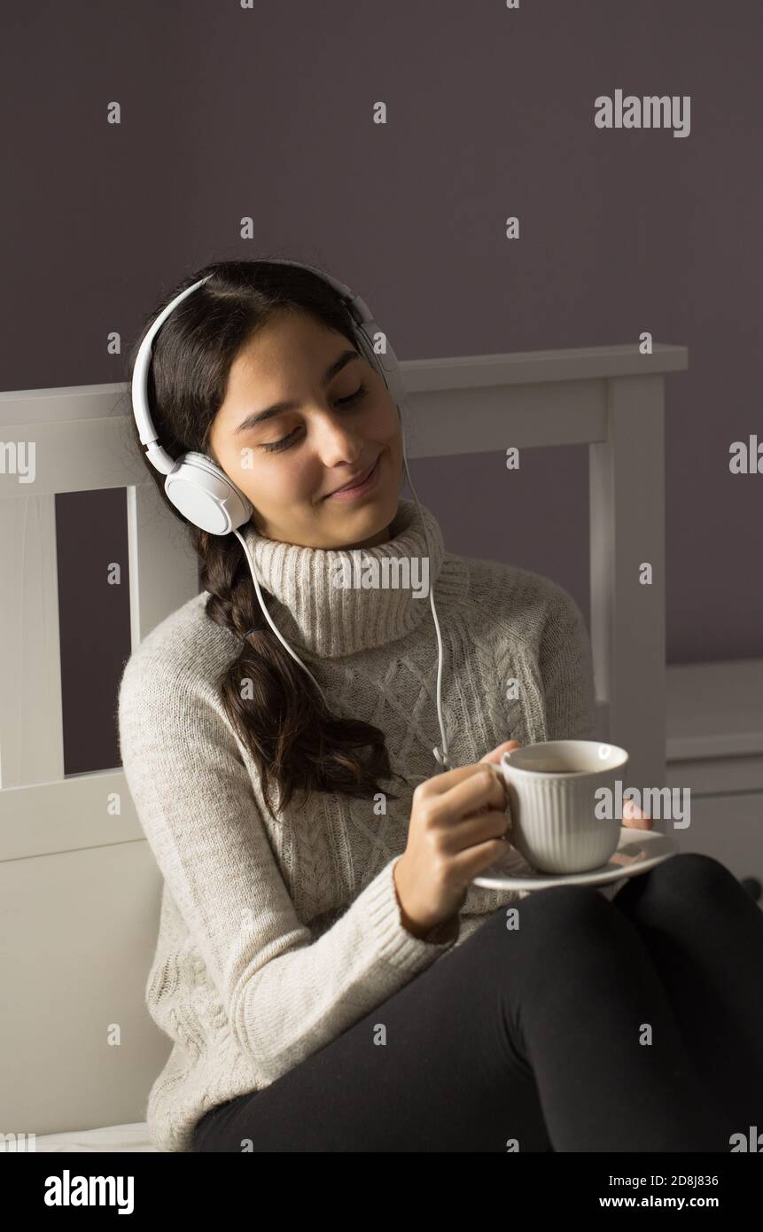 Adolescente a letto che ascolta musica con cuffie e coppa di tè Foto Stock