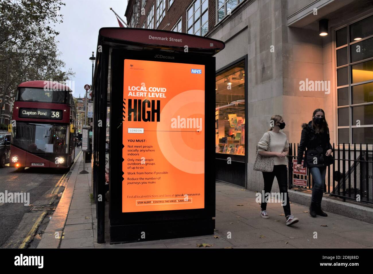 Le persone con maschere facciali passano davanti a un cartello Local Covid Alert Level High nel centro di Londra. Il governo britannico ha introdotto un nuovo sistema a tre livelli con restrizioni in aumento a seconda dei livelli in ciascuna area. Foto Stock