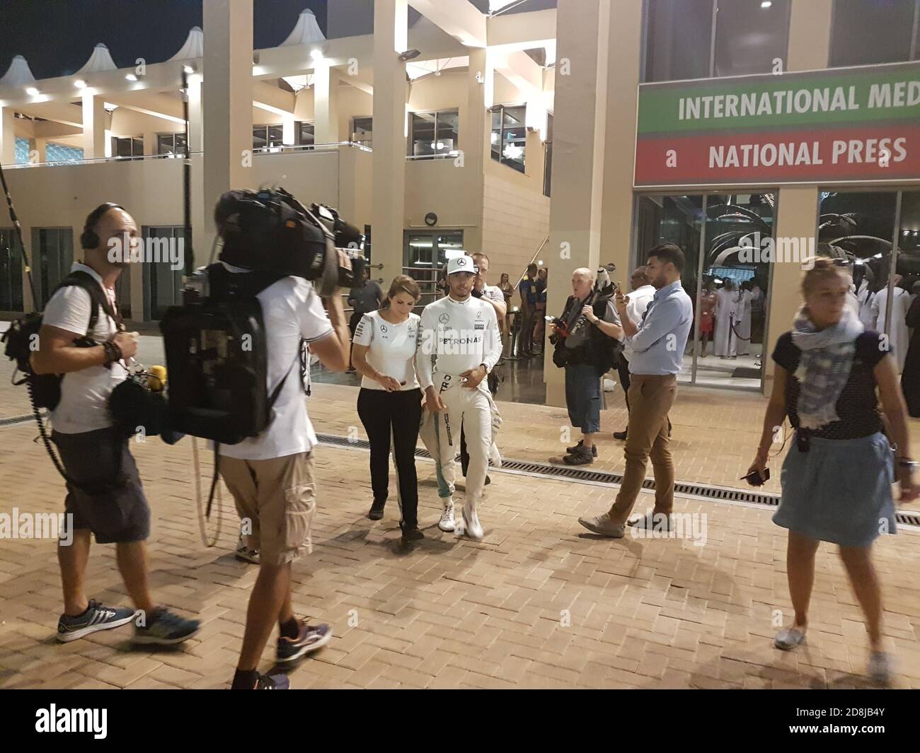 Lewis Hamilton e il personale PR femminile vanno allo stand intervista, dopo la gara, circondato dai media, vicino al Media Center al circuito di Yas Marina Foto Stock