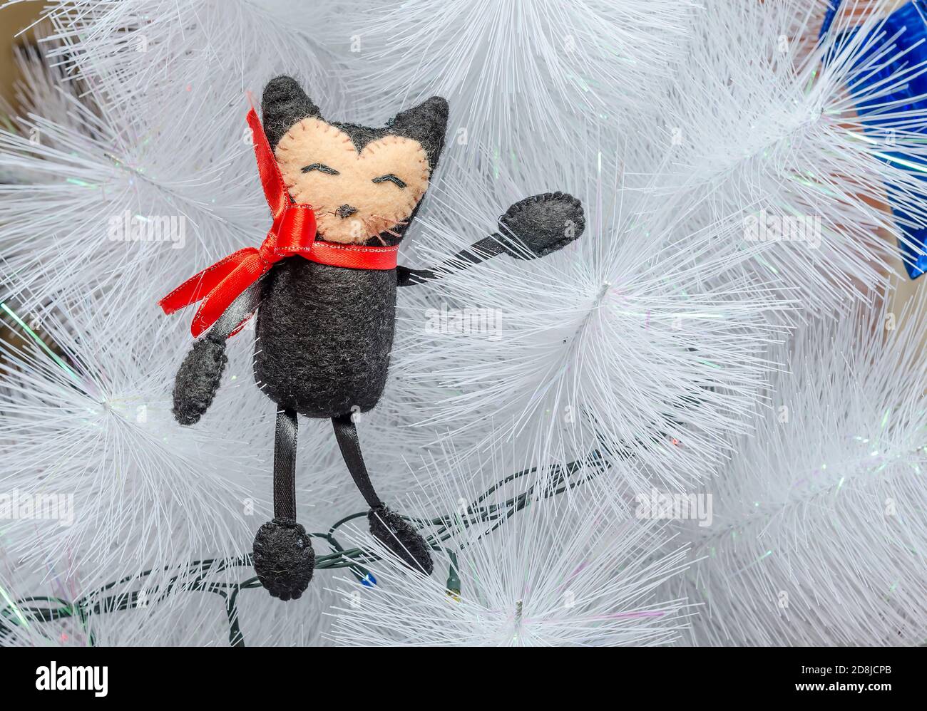 Giocattolo fatto a mano sotto forma di gatto sullo sfondo di un albero di Natale bianco. Capodanno e Natale decorazione Foto Stock