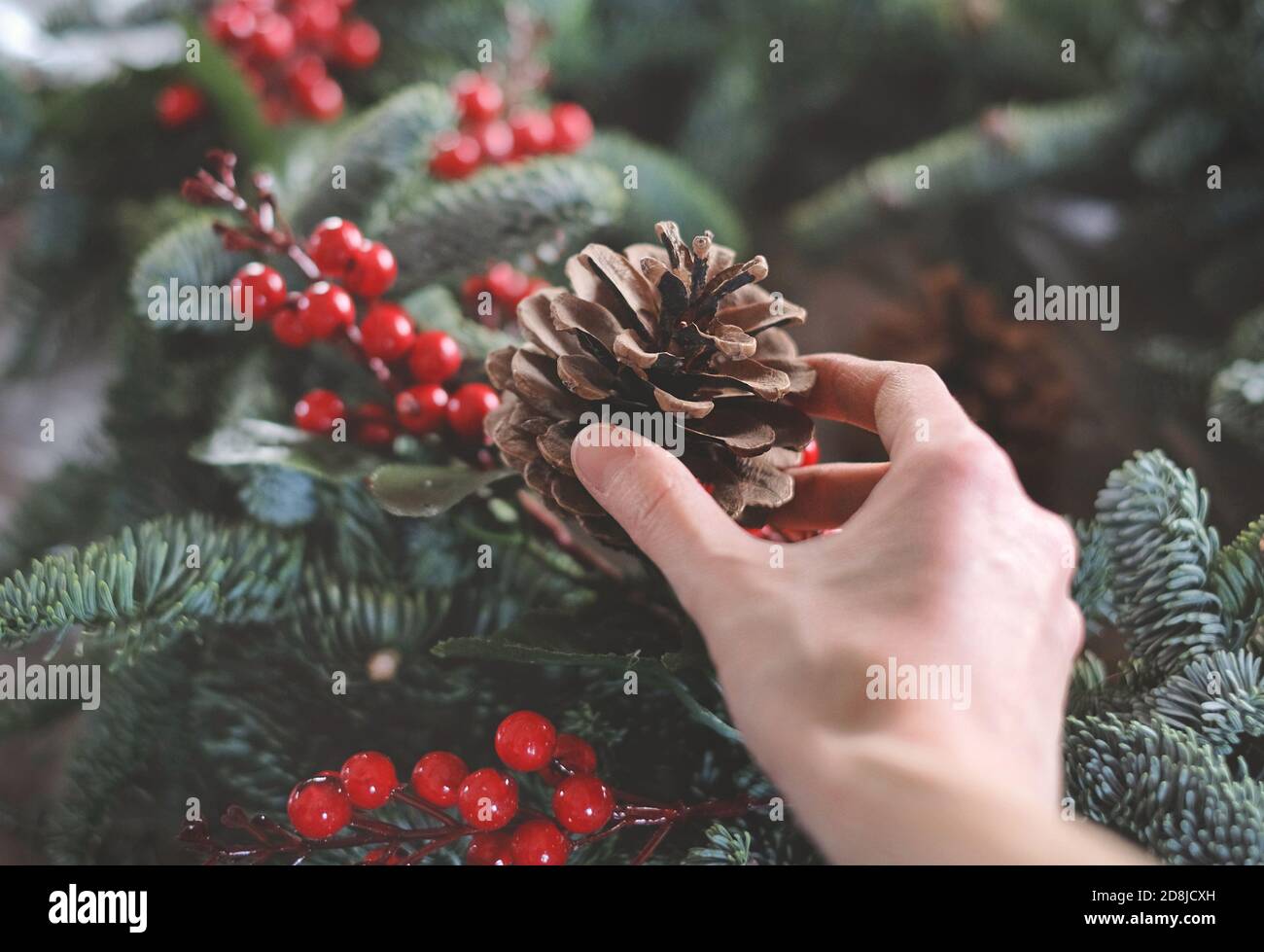 fare la corona di natale con rami di abete e decorazioni. Cono in una mano Foto Stock